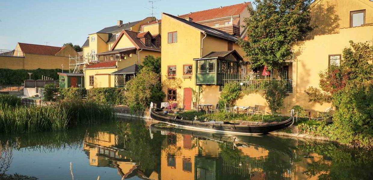 Gemütliche, gelbe Gebäude liegen in der Sonne auf der anderen Seite des Kanals in Frederiksværk