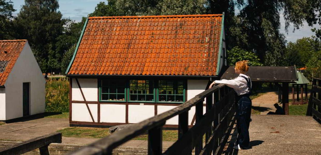 Eine junge Frau steht auf einer Brücke und betrachtet ein kleines Fachwerkhaus im Pulverwerkmuseum