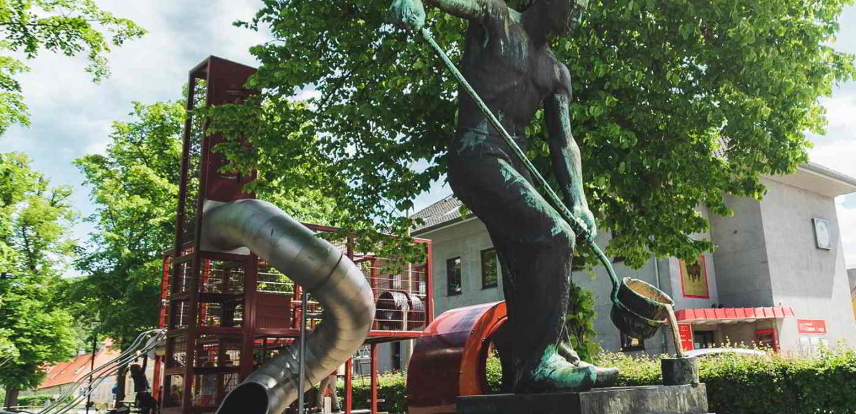 Der Spielplatz in Frederiksværk mit der großen Rutsche im Hintergrund und einer Statue eines Arbeiters im Vordergrund.