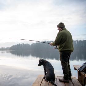 Mand og hund fisker ved en sø og kigger efter tang på en fiskekrog