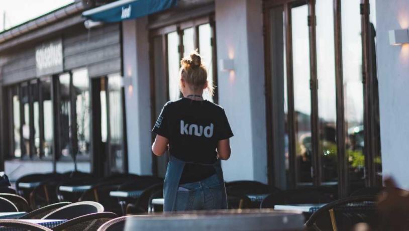 Ein Kellner ist bereit zum Servieren in der Morgensonne auf der Terrasse vor dem Restaurant Knud in Hundested.