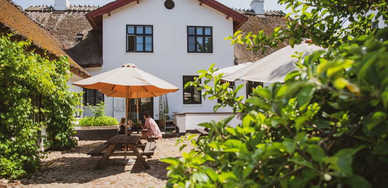 Eine Mutter und ihre Kinder essen unter einem Sonnenschirm im Innenhof des Møllecafé am Esrum Kloster.